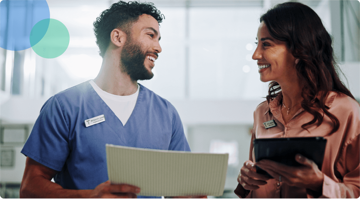Two healthcare workers smiling and reviewing documents together in a bright clinical setting.