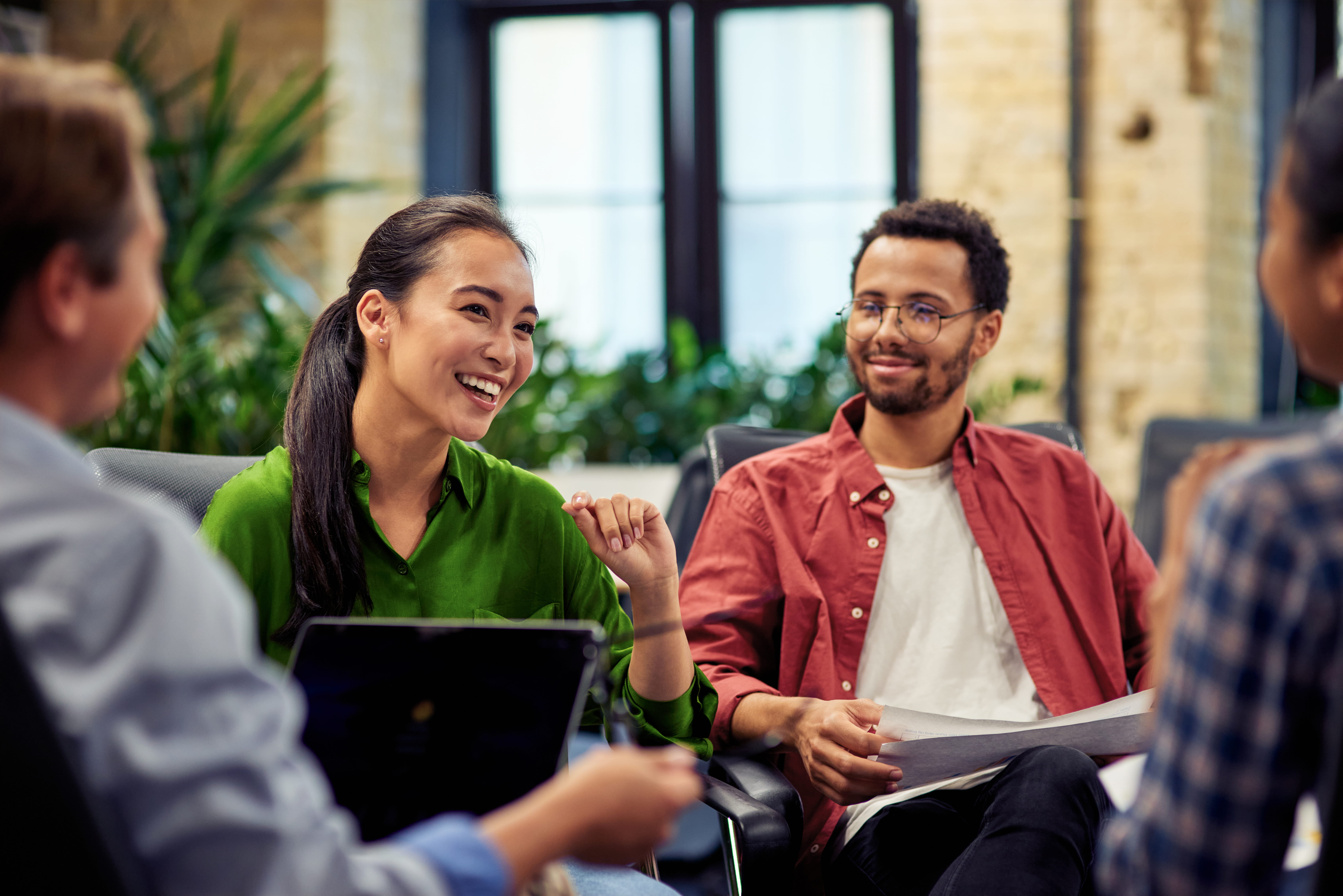 Four diverse coworkers engaged in a friendly discussion in a modern office with plants.
