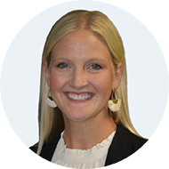 Smiling woman with blonde hair wearing white earrings and a black blazer over a white top.
