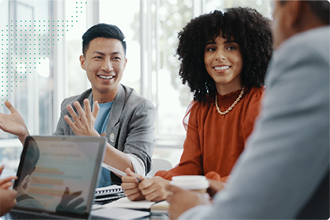 Diverse group in a meeting with a smiling man explaining, a woman listening, and a laptop on the table.