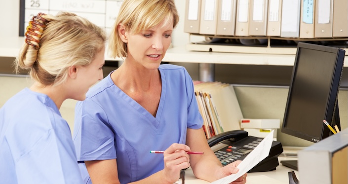 Mature female doctor discussing medical report with nurses in hospital hallway