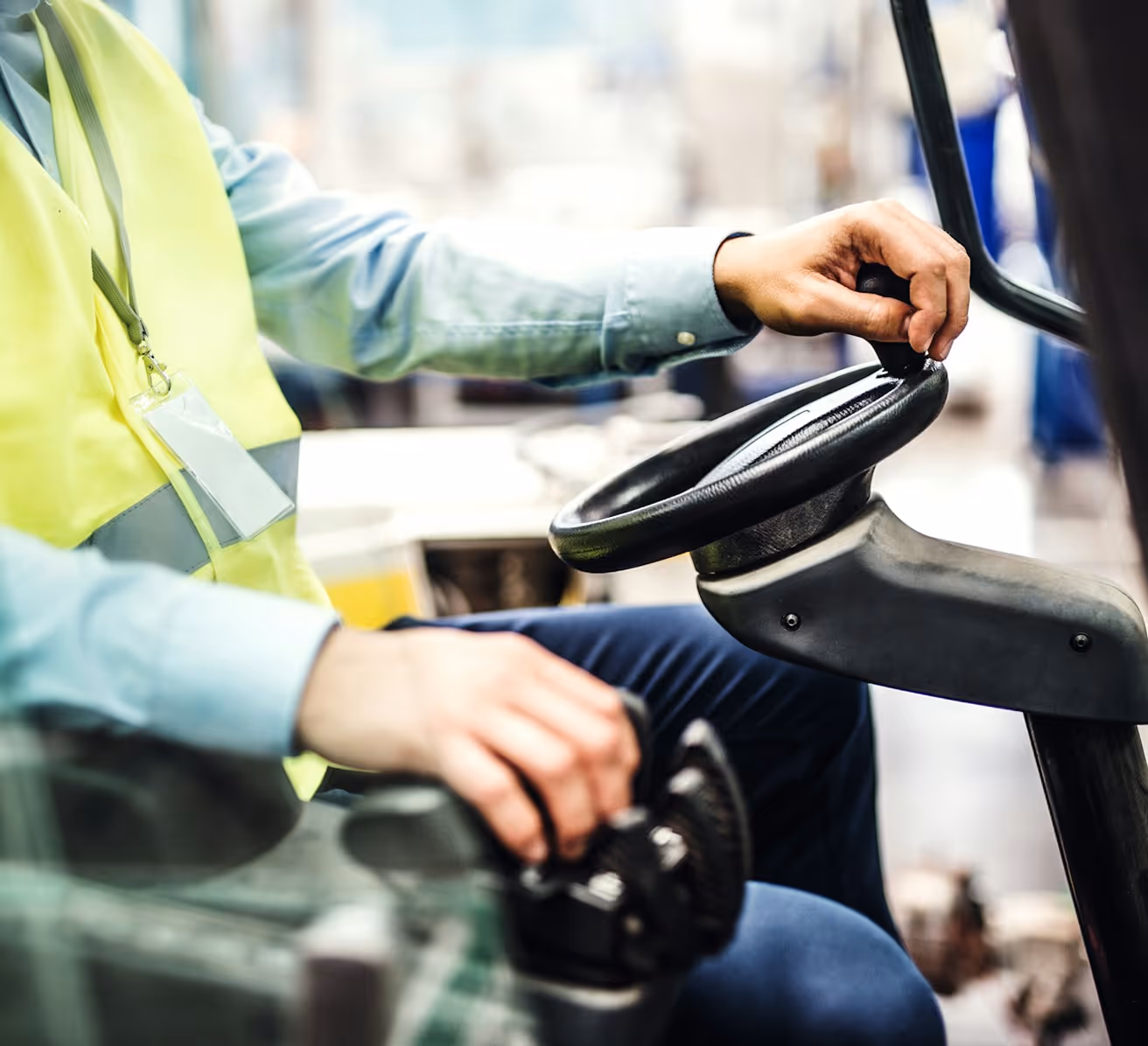 Arbeiter in Warnweste bedient Lenkrad und Steuerhebel in einem Fahrzeug oder Gerät.
