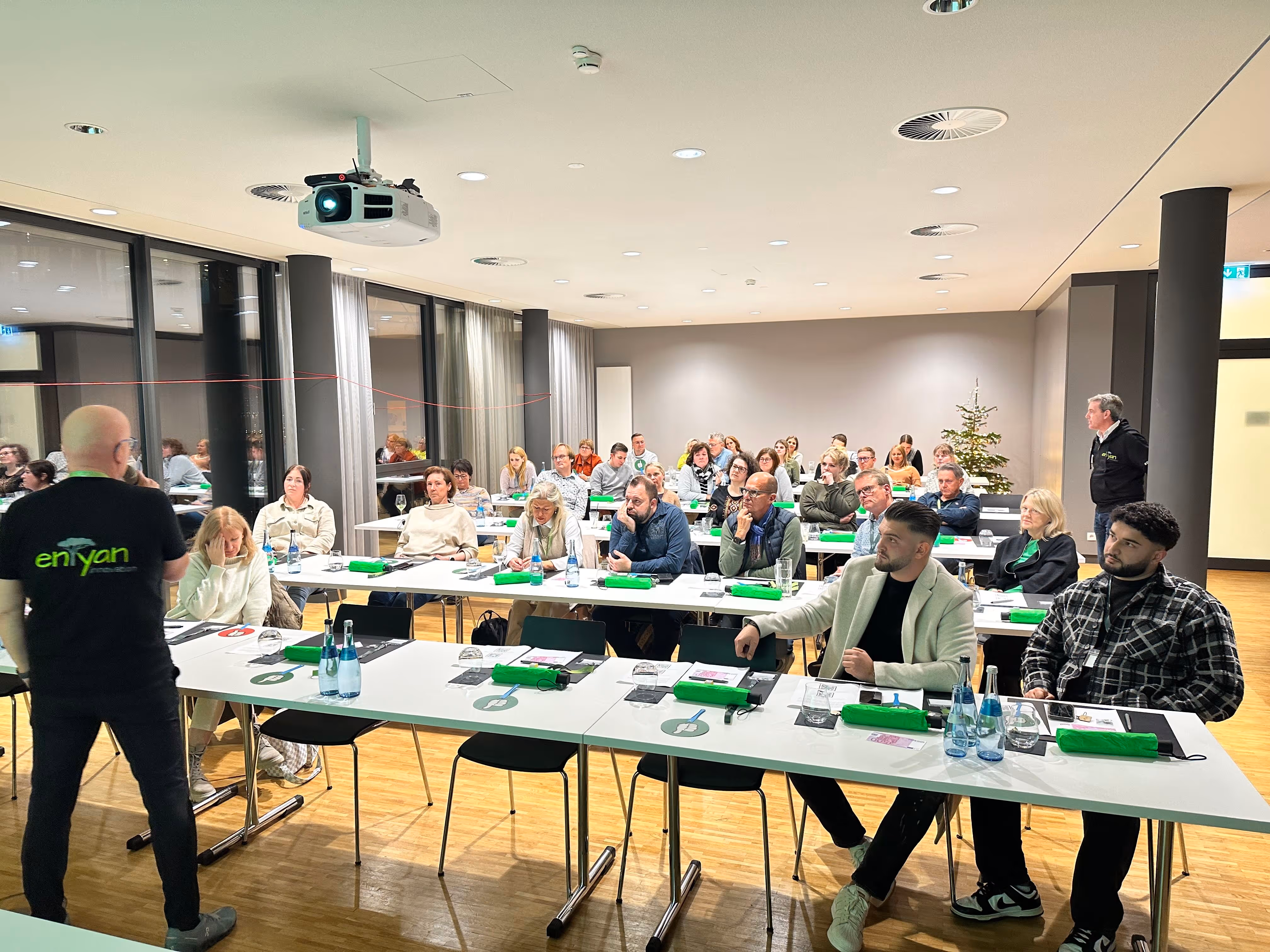 Teilnehmende eines Eniyan-Seminars sitzen in einem modernen Konferenzraum und hören einer Präsentation über digitale Lösungen zu.