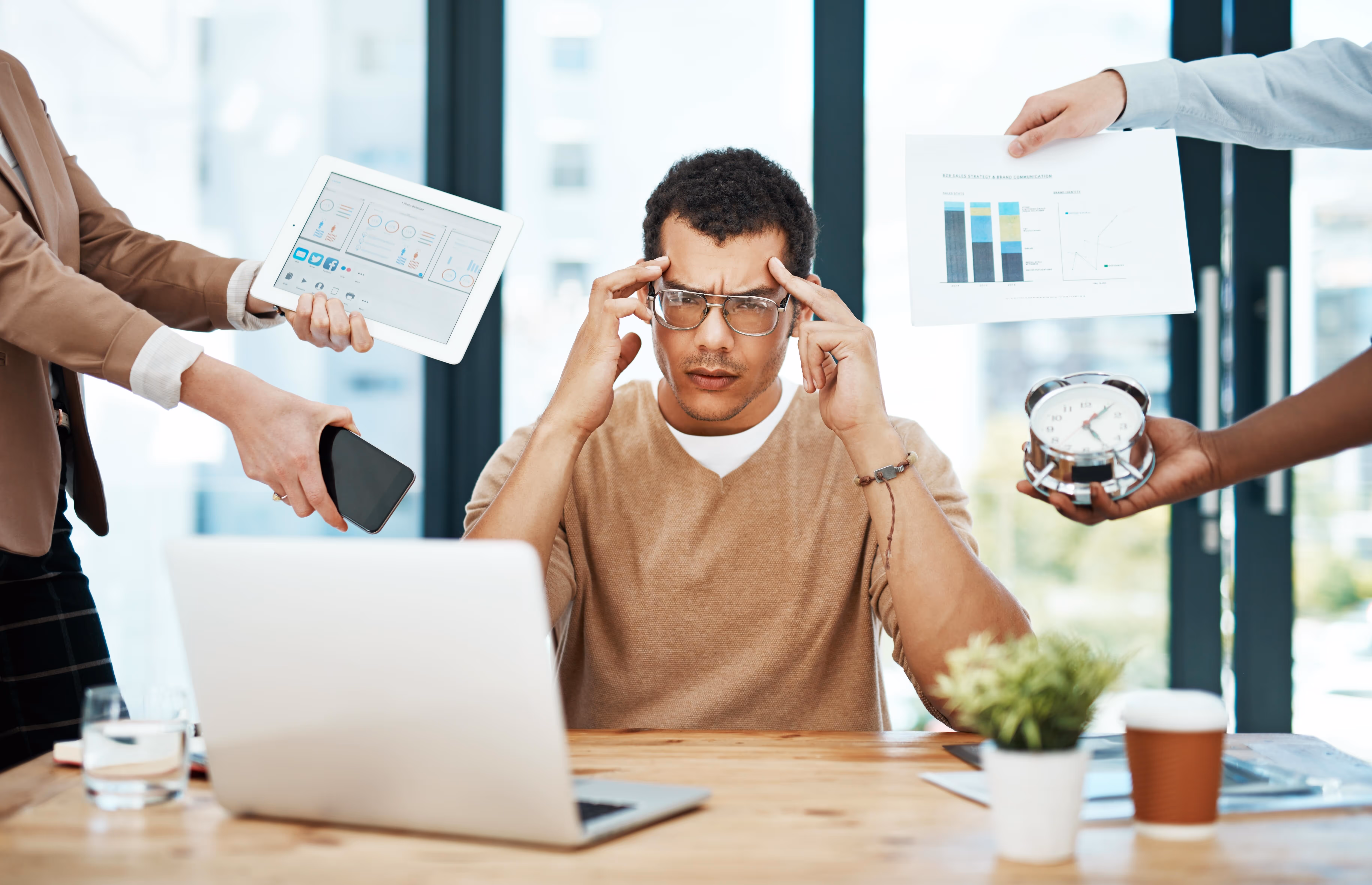 Gestresste Person im Büro mit Laptop, Uhr und Diagrammen – Symbol für digitale Überlastung im Reisebüro vor der Digitalisierung