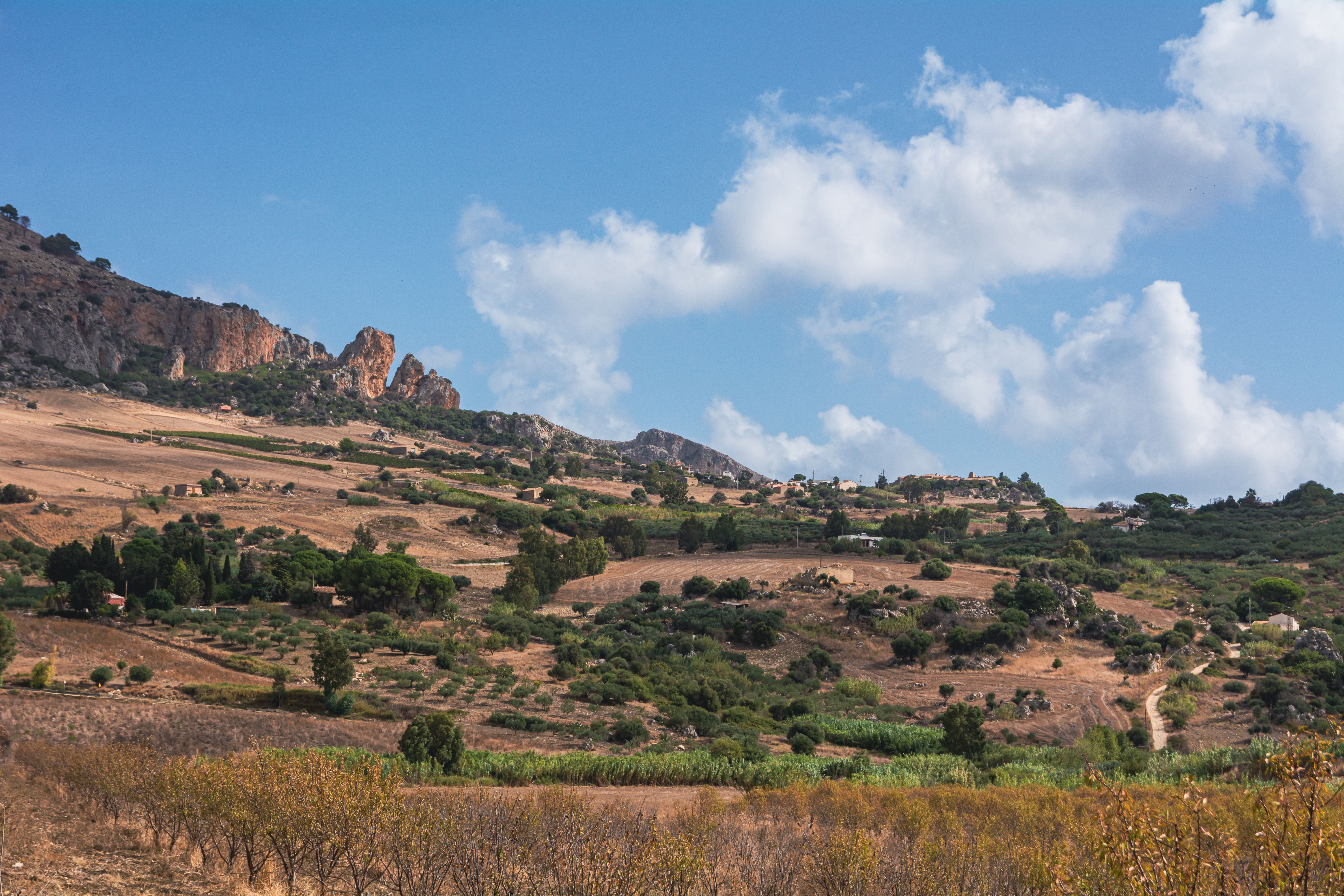 Scenic view of rolling hills and farmland with clear blue sky and fluffy clouds.