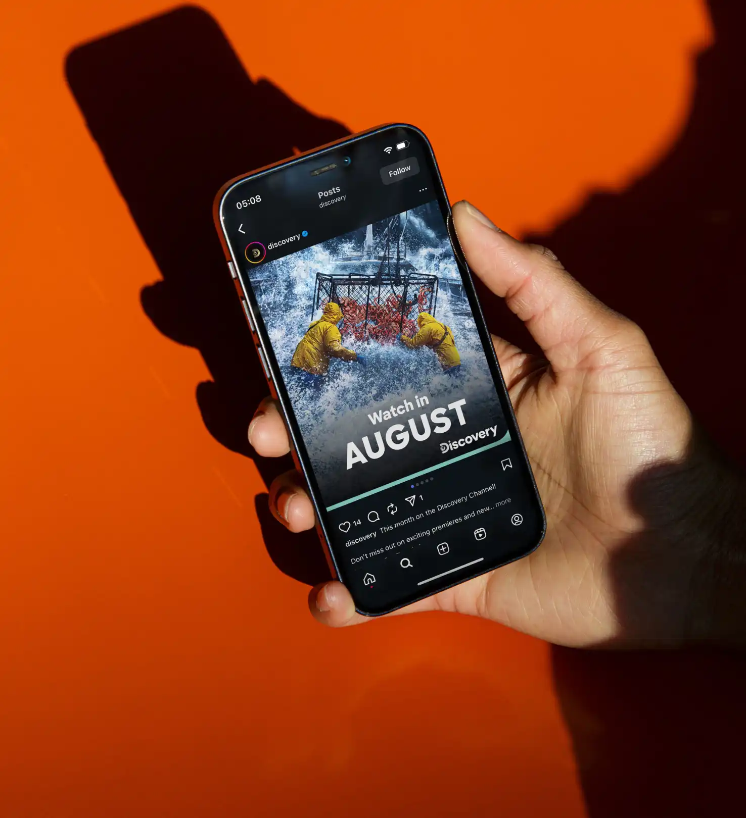 Forleap Marketing. Warner Bros Discovery cover image case study. Hand holding a smartphone displaying a Discovery Instagram post about shows to watch in August, with an image of two people in yellow rain jackets pulling a crab pot in rough waters.
