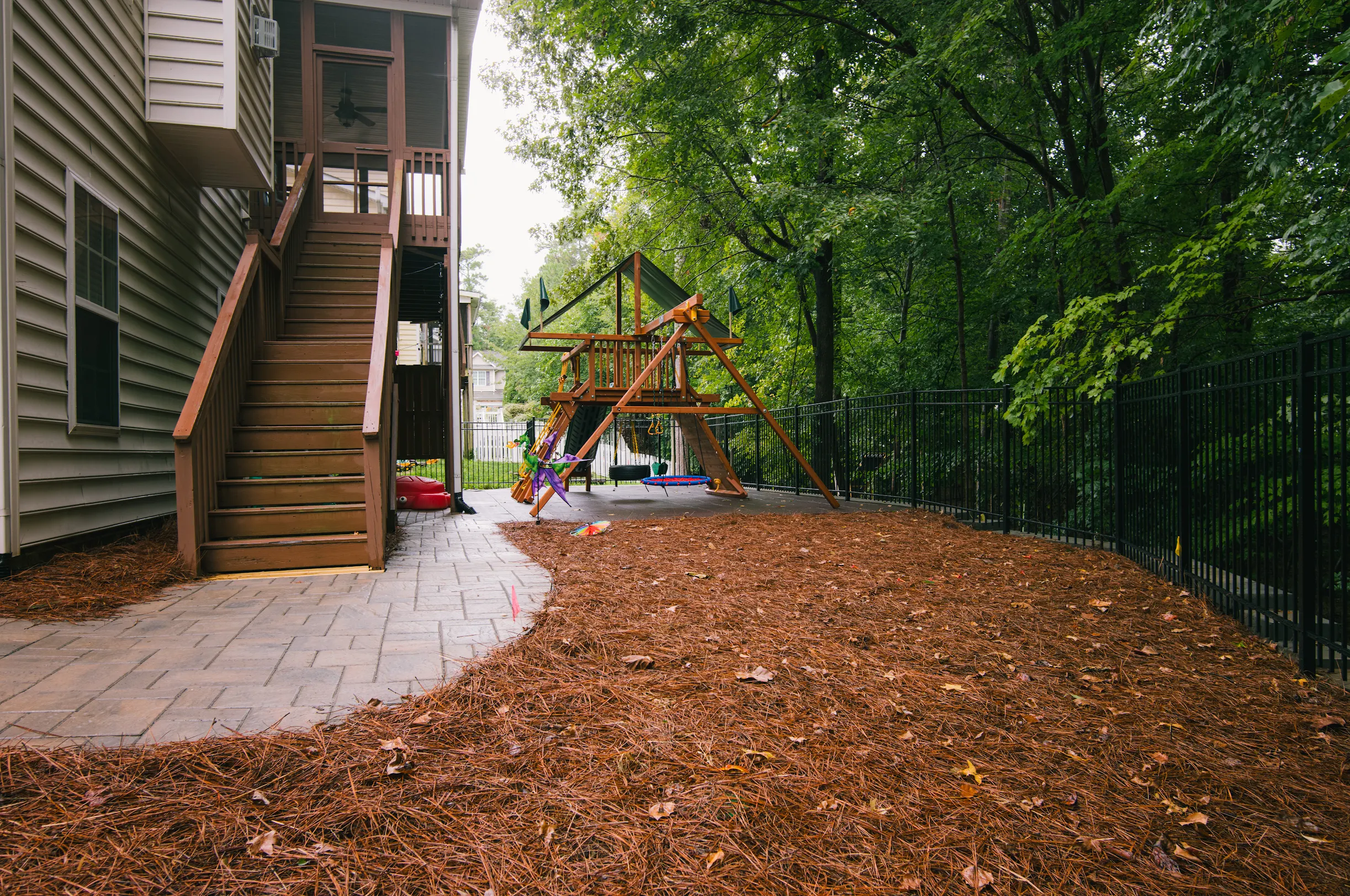 Wooden swing set in backyard with mulch ground and stone patio