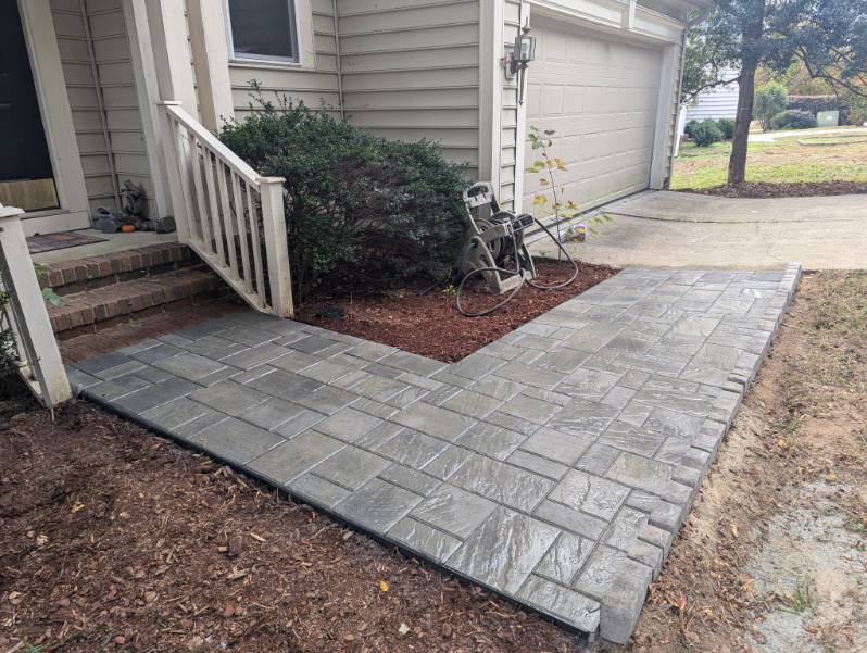 Newly installed gray stamped concrete walkway with a stone pattern leading to a house entrance and garage.