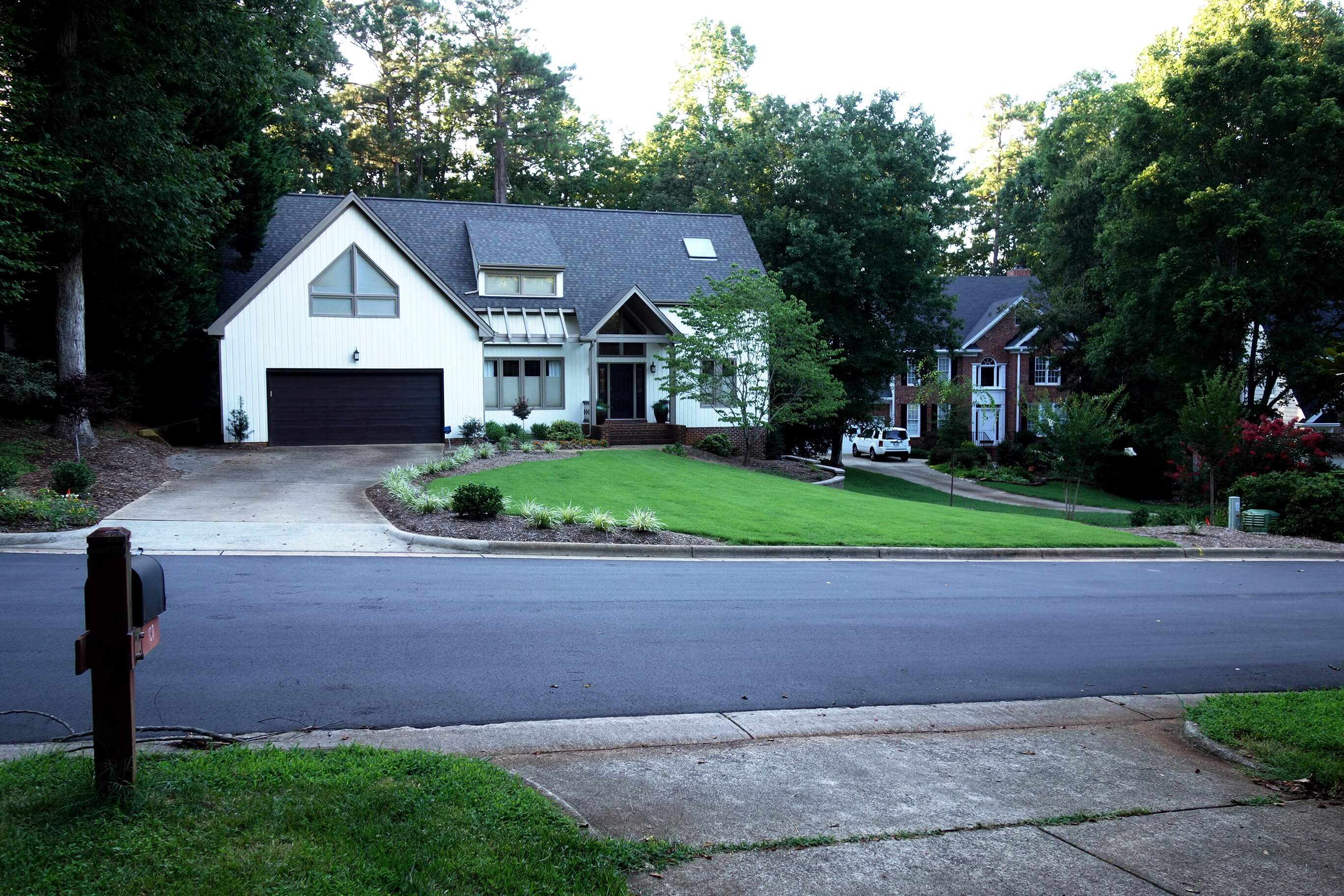 Modern white house with a black garage door, surrounded by green lawn and trees.