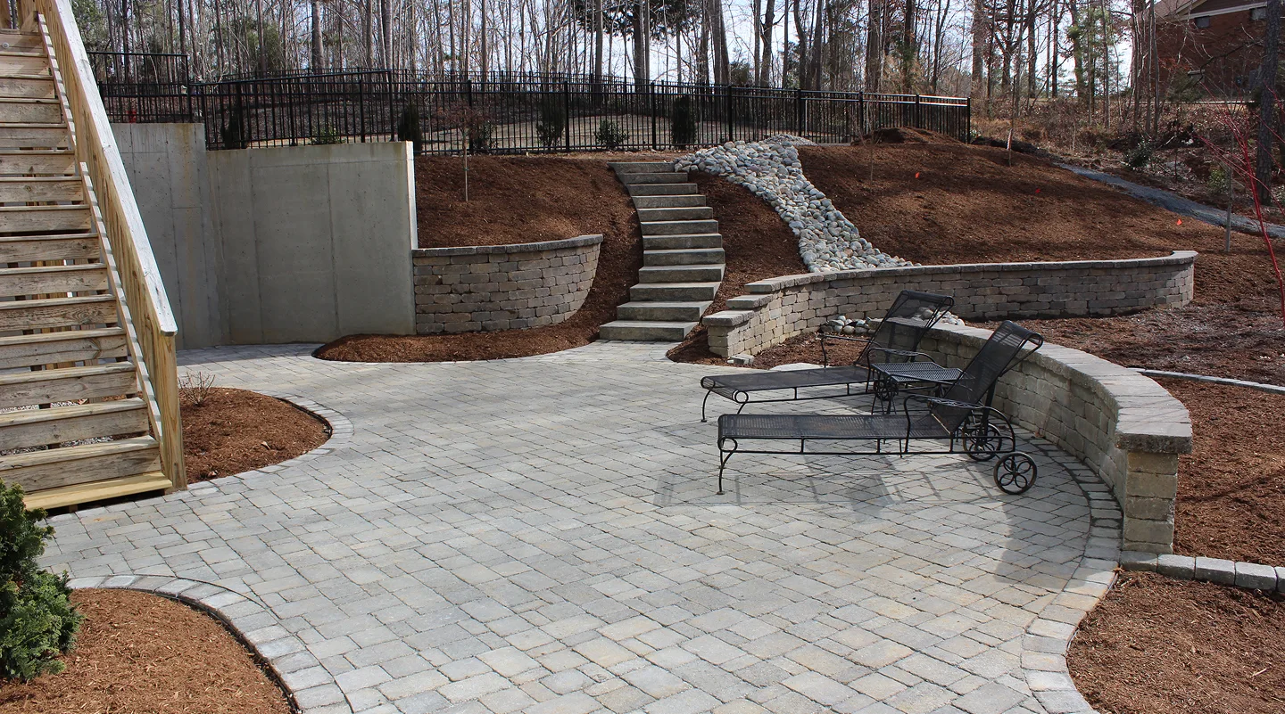 A cozy patio with a bench and steps that rise toward a hillside, surrounded by greenery.
