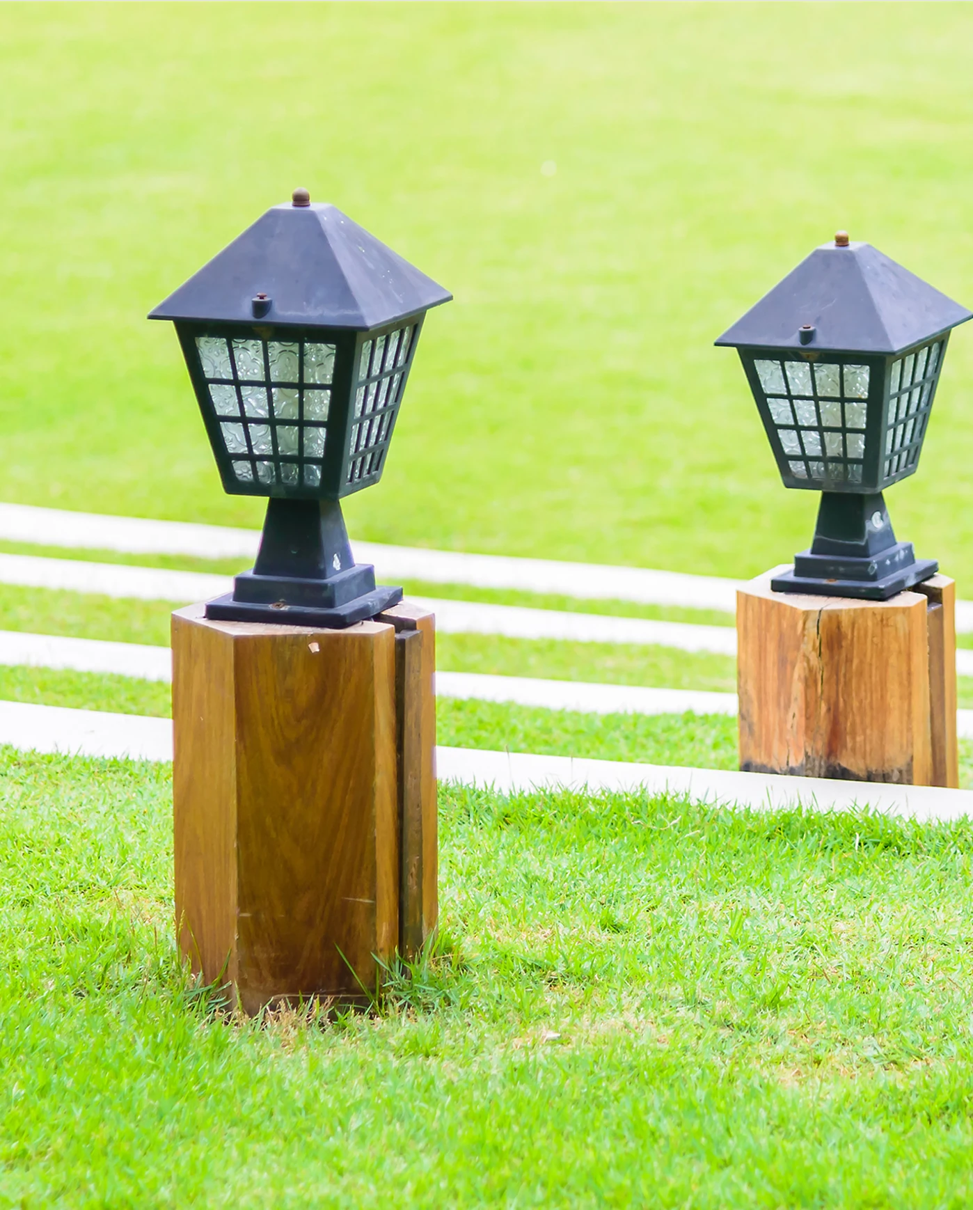 Two black lamps on wooden posts in a grassy field.