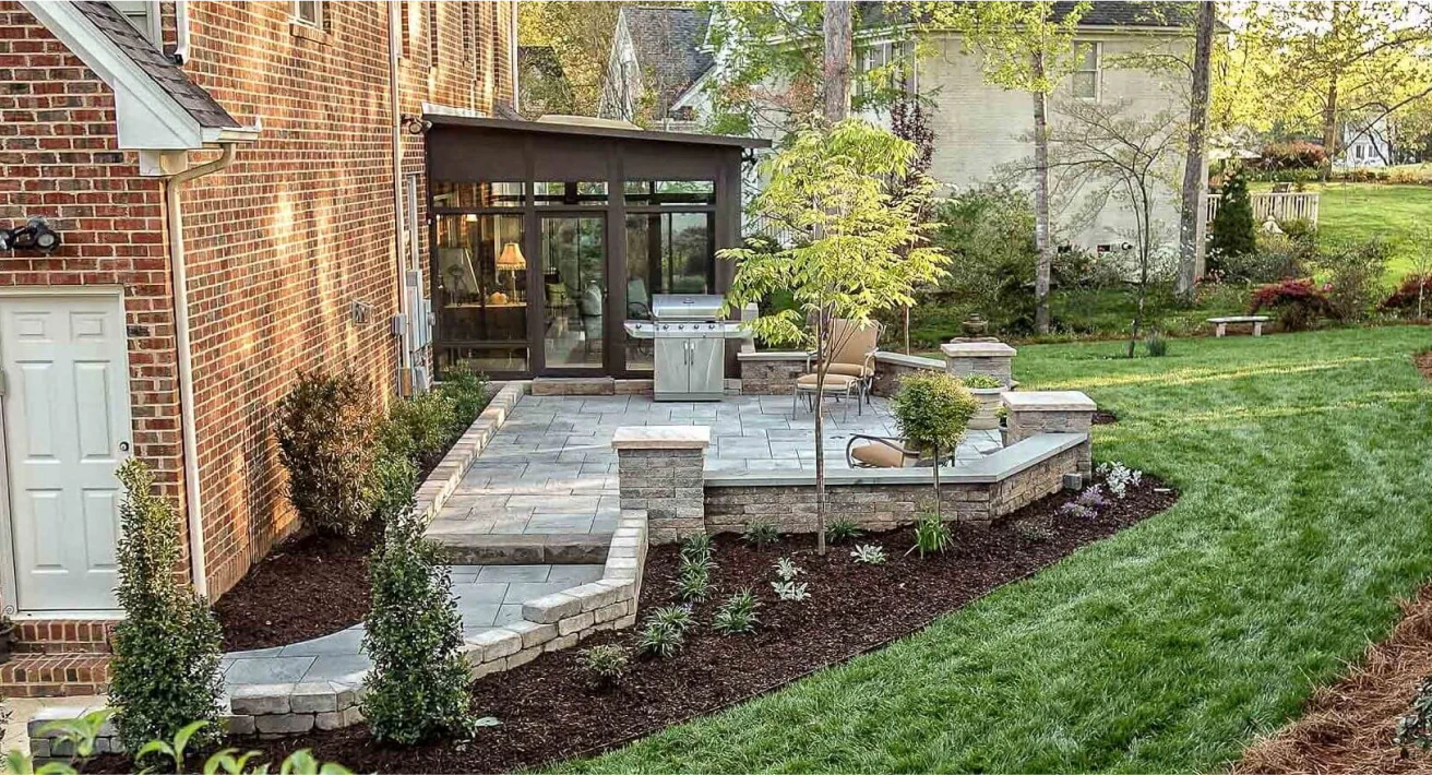 A backyard patio with a grill and a tree.