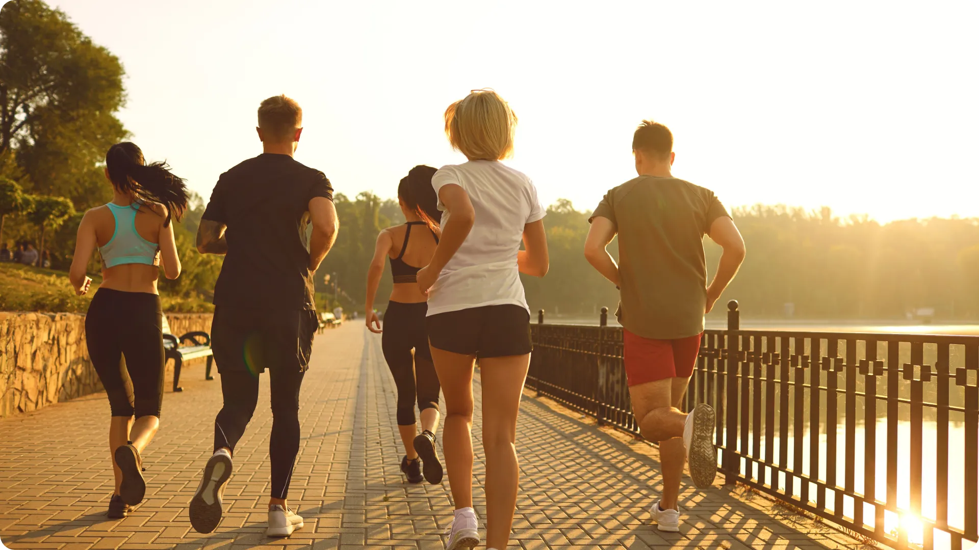 Diverse group of runners exercising together along urban waterfront at sunrise, representing fitness community as social activity and wellness optimization