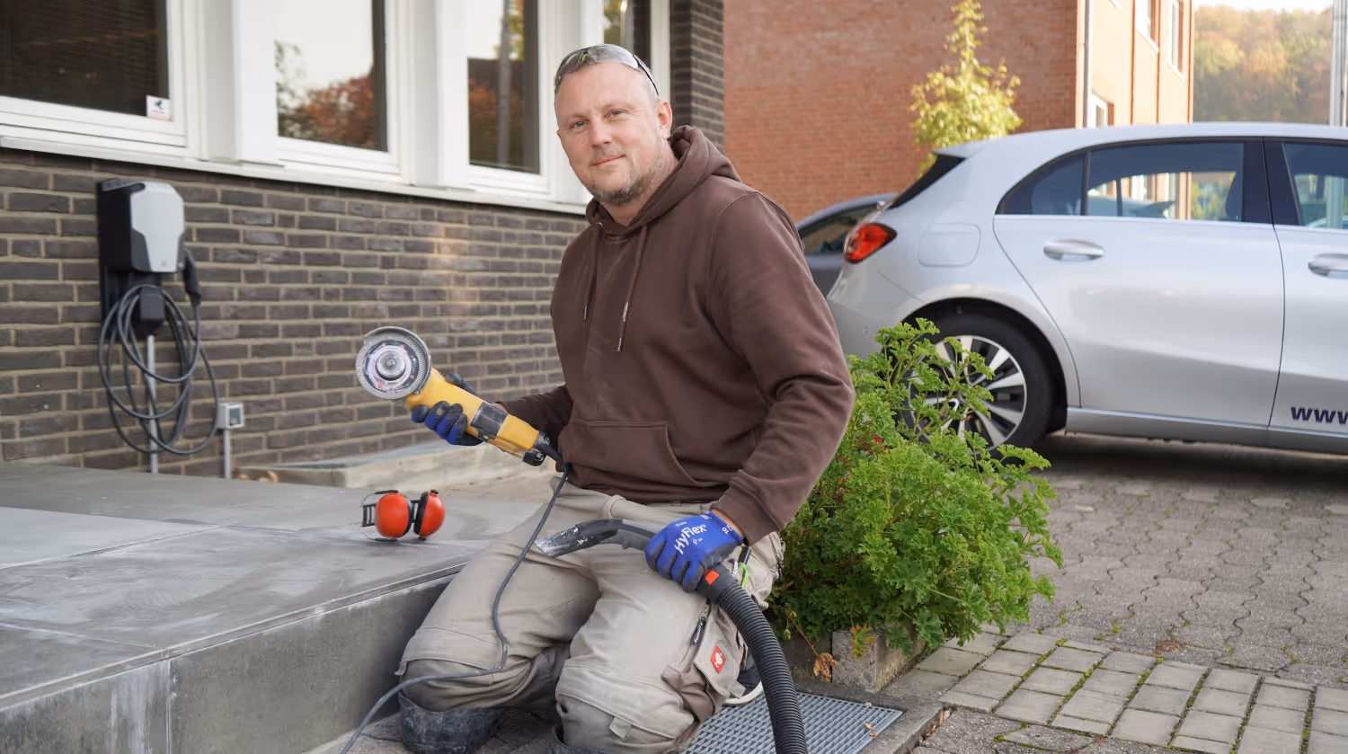 Gast Mitarbeiter sitzt mit Flex vor einem Hauseingang.