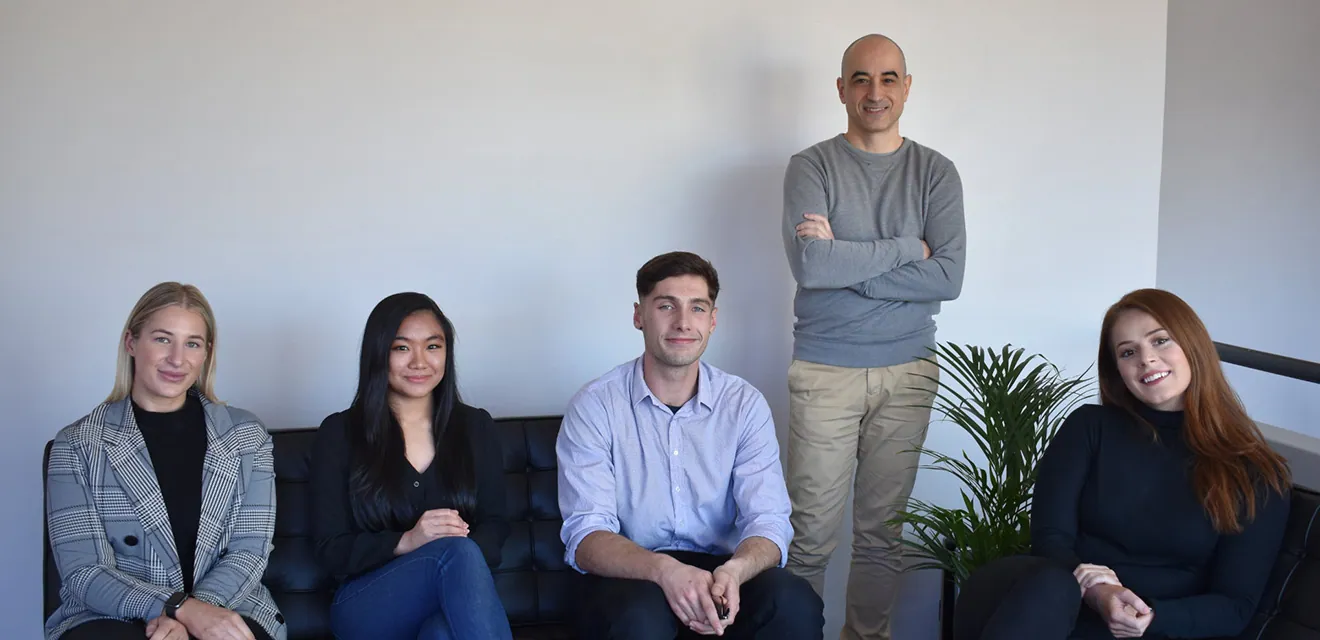 Team of five Ambire employees in the office - four sitting on a couch, one standing behind