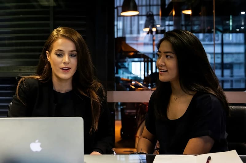 Two women collaborating at a modern office workspace, both engaged in discussion
