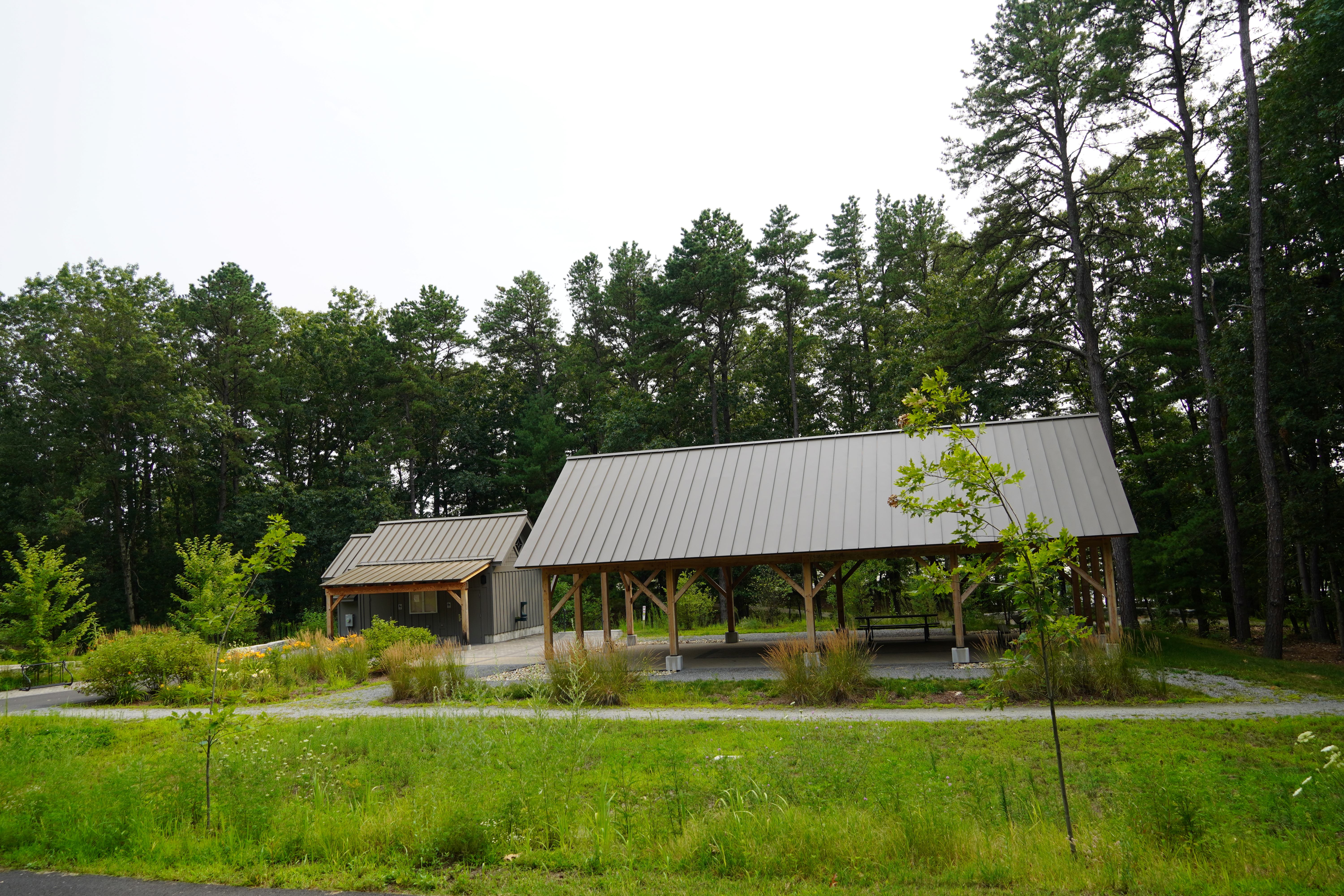 this picture shows a small pavilion with picnic tables underneath, as well as a small bathroom building to the left
