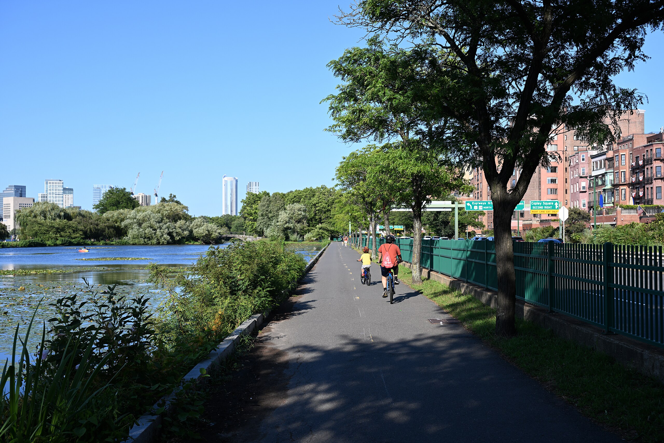 this photo shows the trail going alongside storrow drive through Back Bay. Brownstones can be seen on the right side over the road, while the left side shows the river