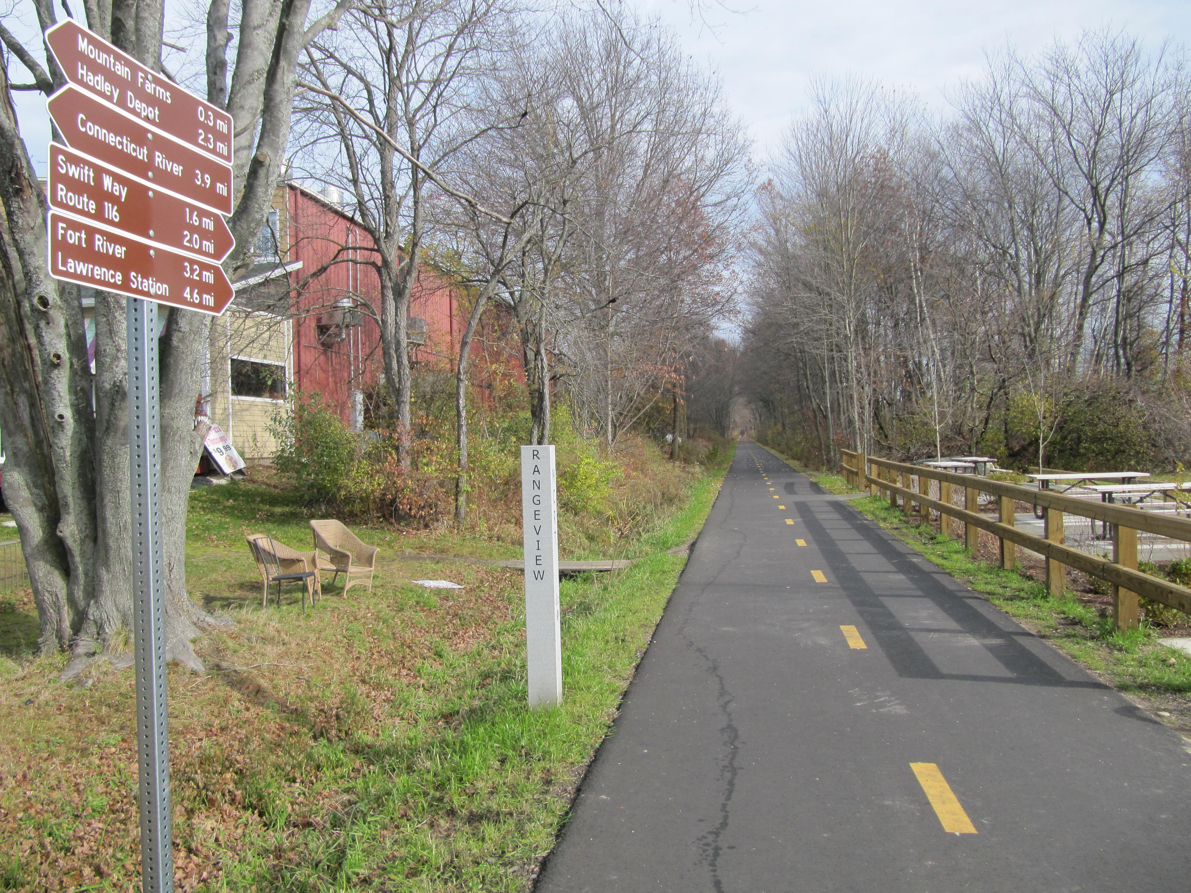 this image shows a view of the trail in hadley. on the right theres a rest area with picnic tables. on the right theres a navigational sign