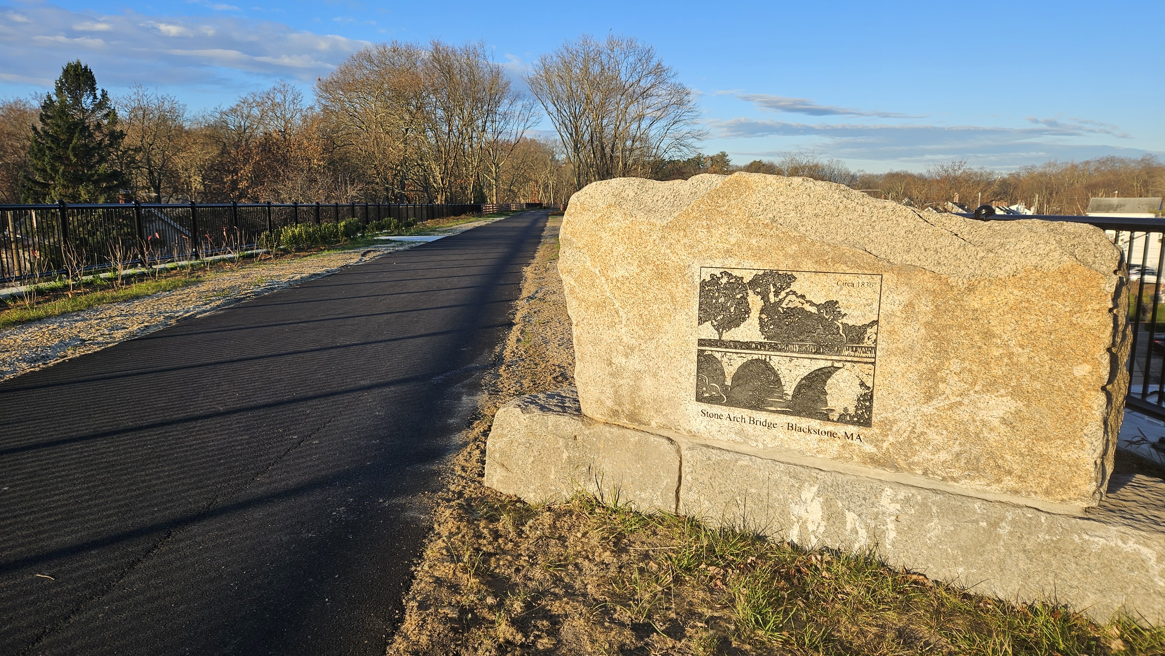 a view going over the blackstone viaduct. there is a stone marker with an engraved marking on it on the right that shows the original version of the stone bridge