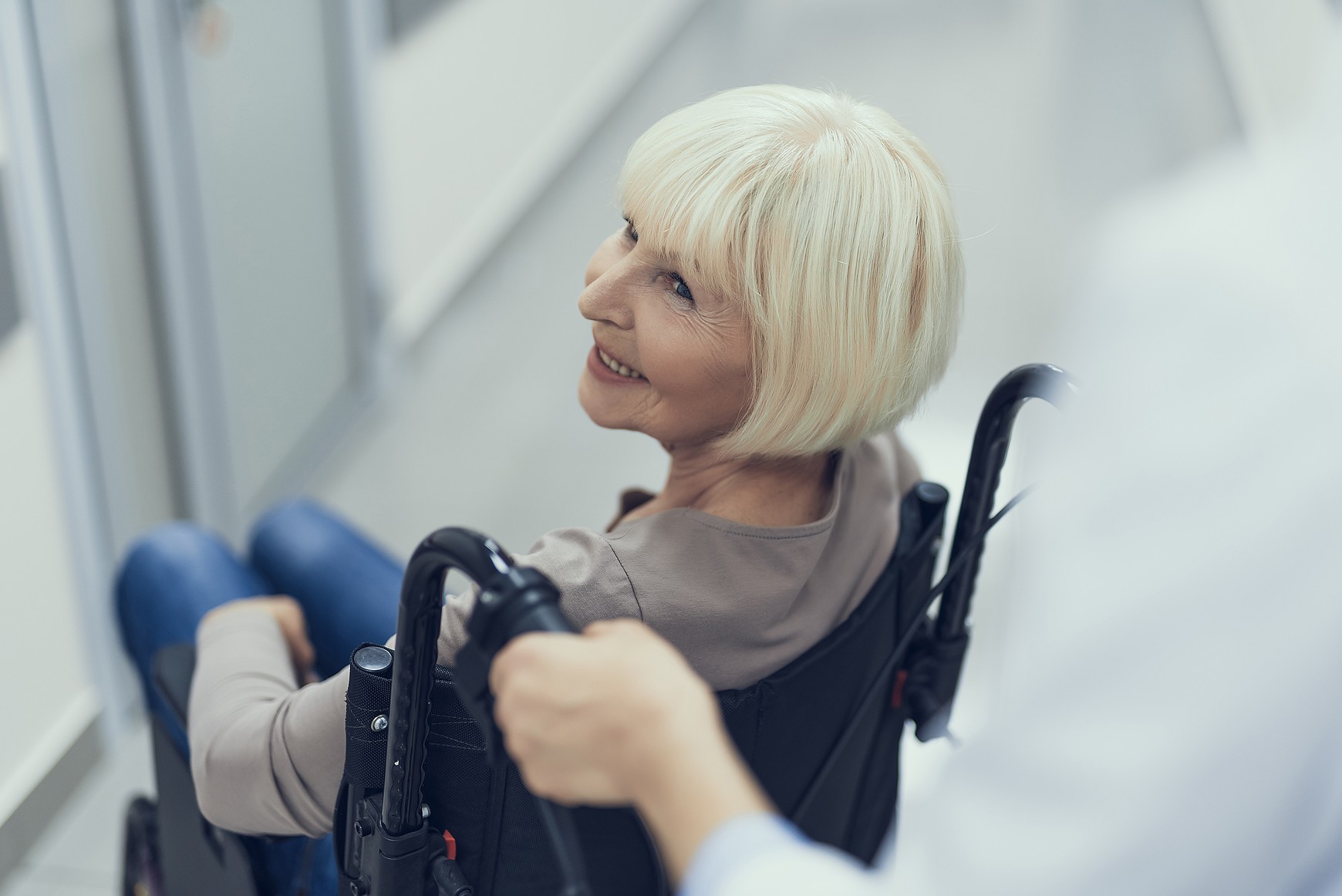 A smiling woman in a wheelchair being assisted by a member of the care team