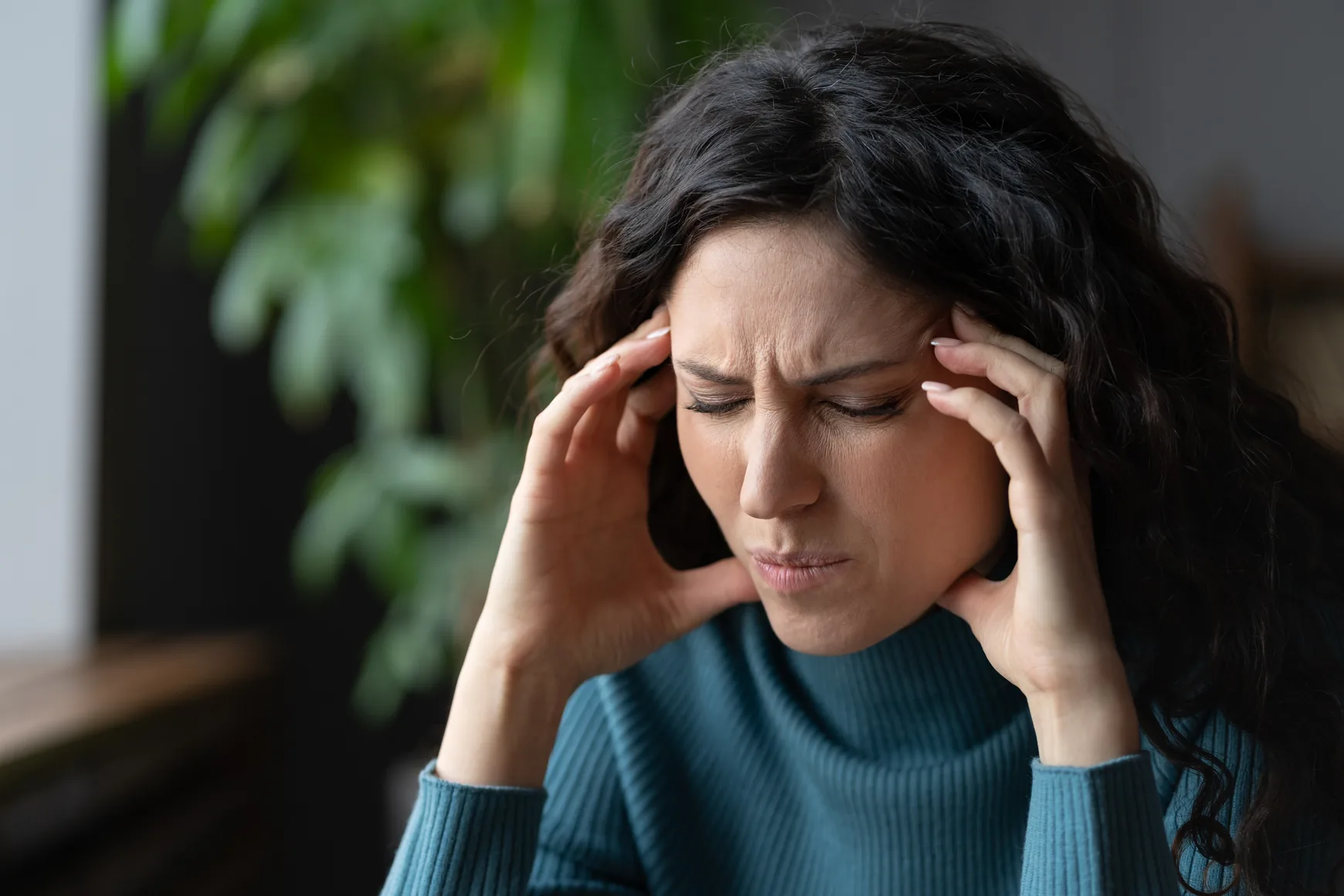 A woman sitting indoors with a headache, resting her fingers against her temples