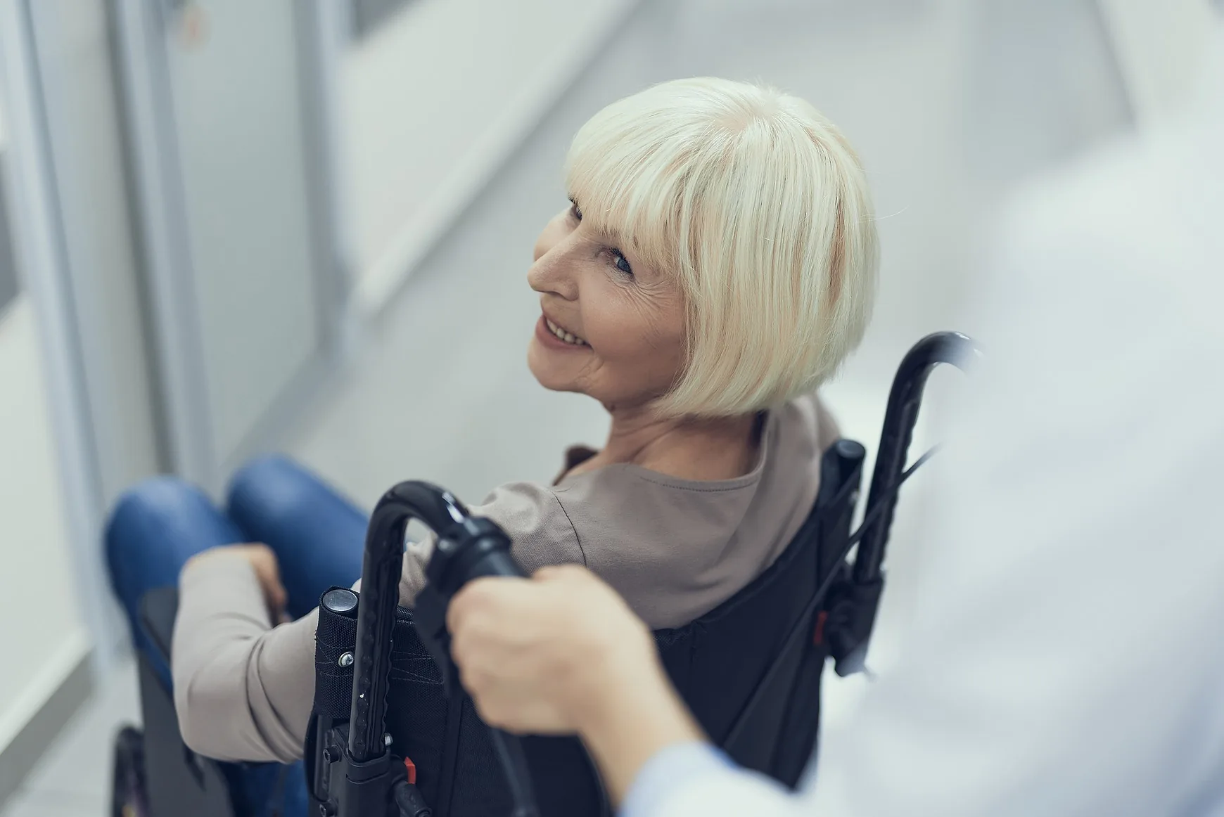 A smiling woman in a wheelchair being assisted by a member of the care team