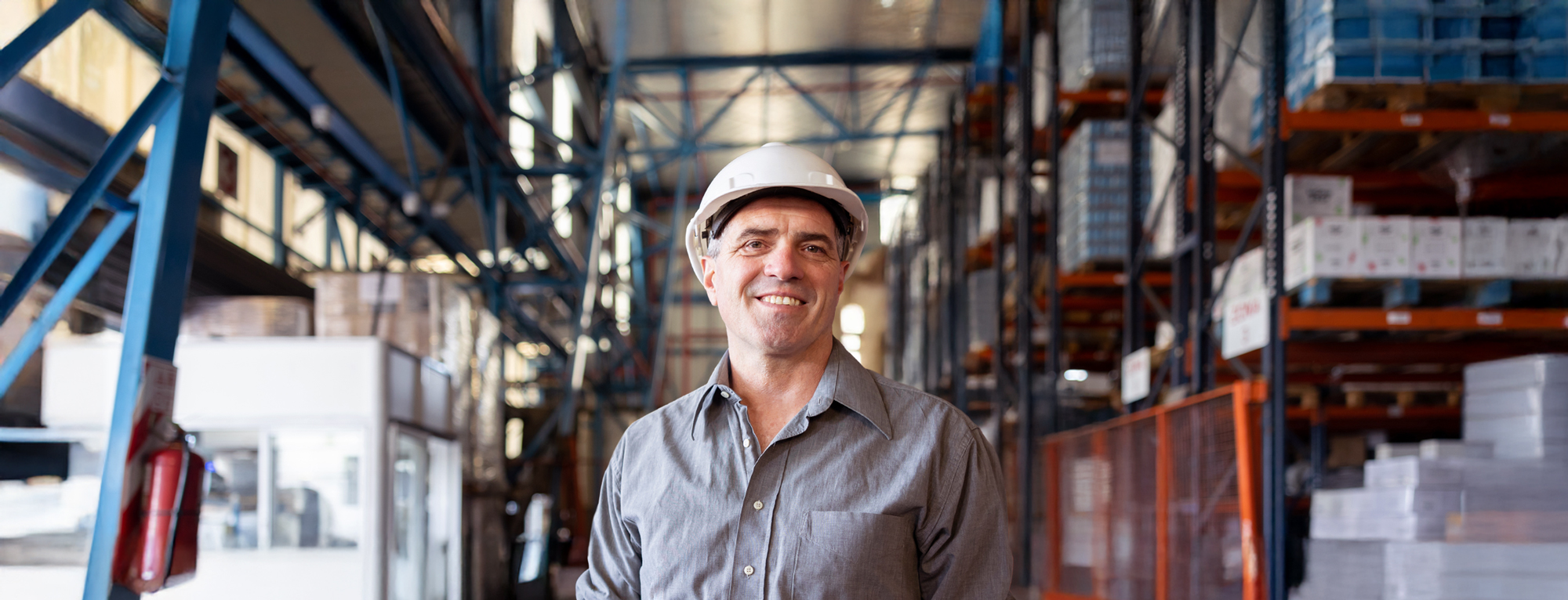 A smiling man wearing a hard hat stands in a warehouse.