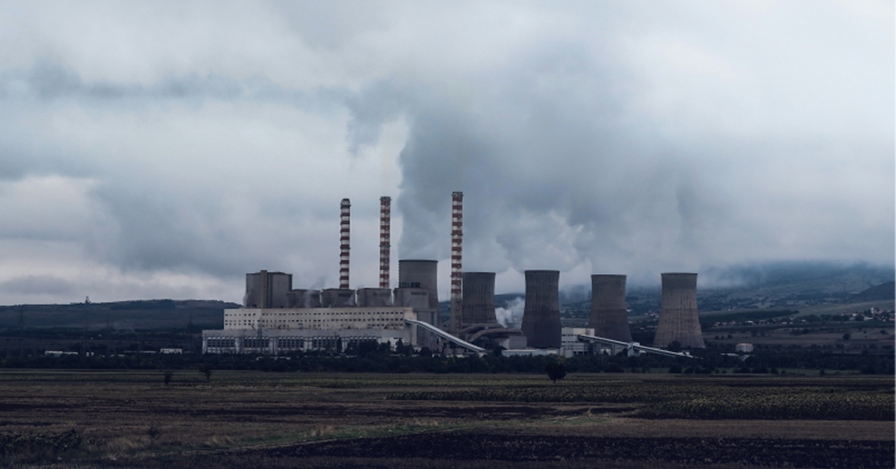 Industrial power plant with several cooling towers and smokestacks emitting steam under a cloudy sky.