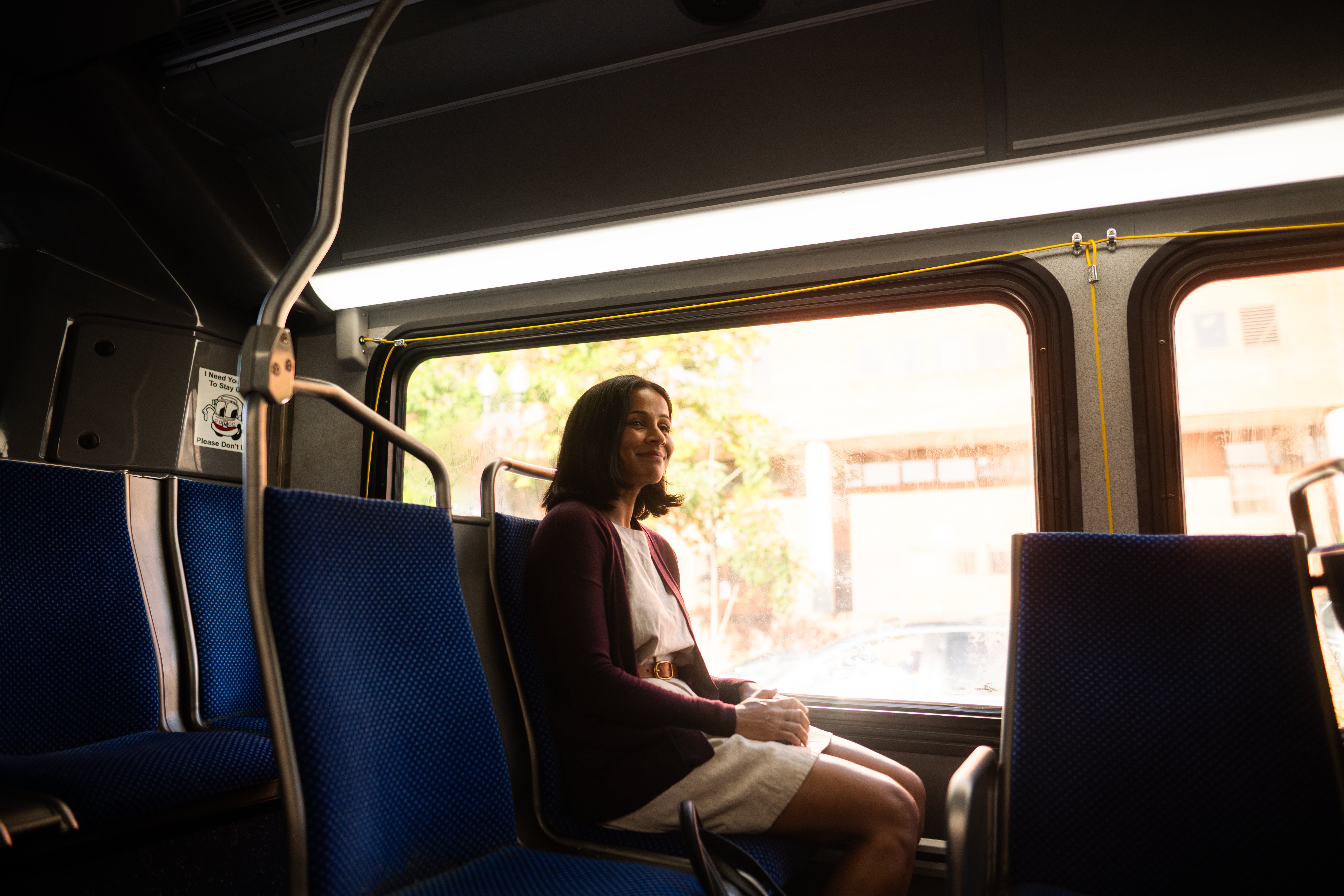 Photo of Aparna sitting on a bus and smiling at some people nearby