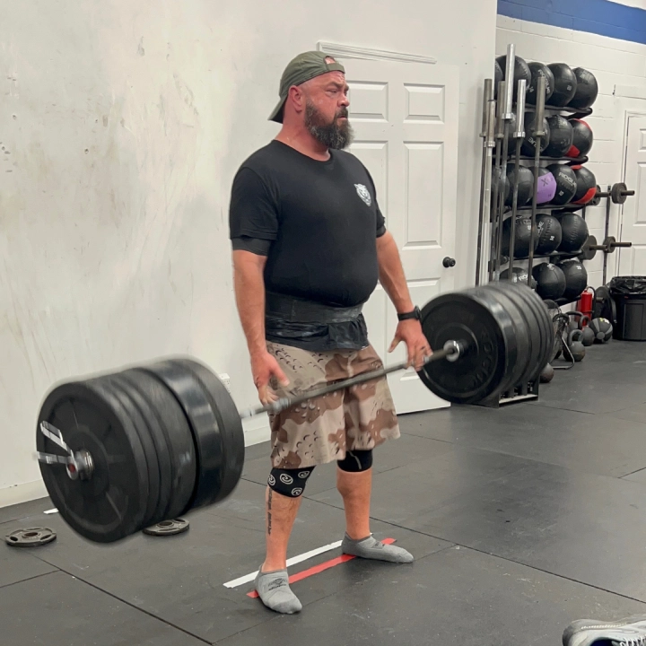 A bearded man stands in a gym at CrossFit Empire South, holding a barbell, ready for his workout in Huntsville, AL.
