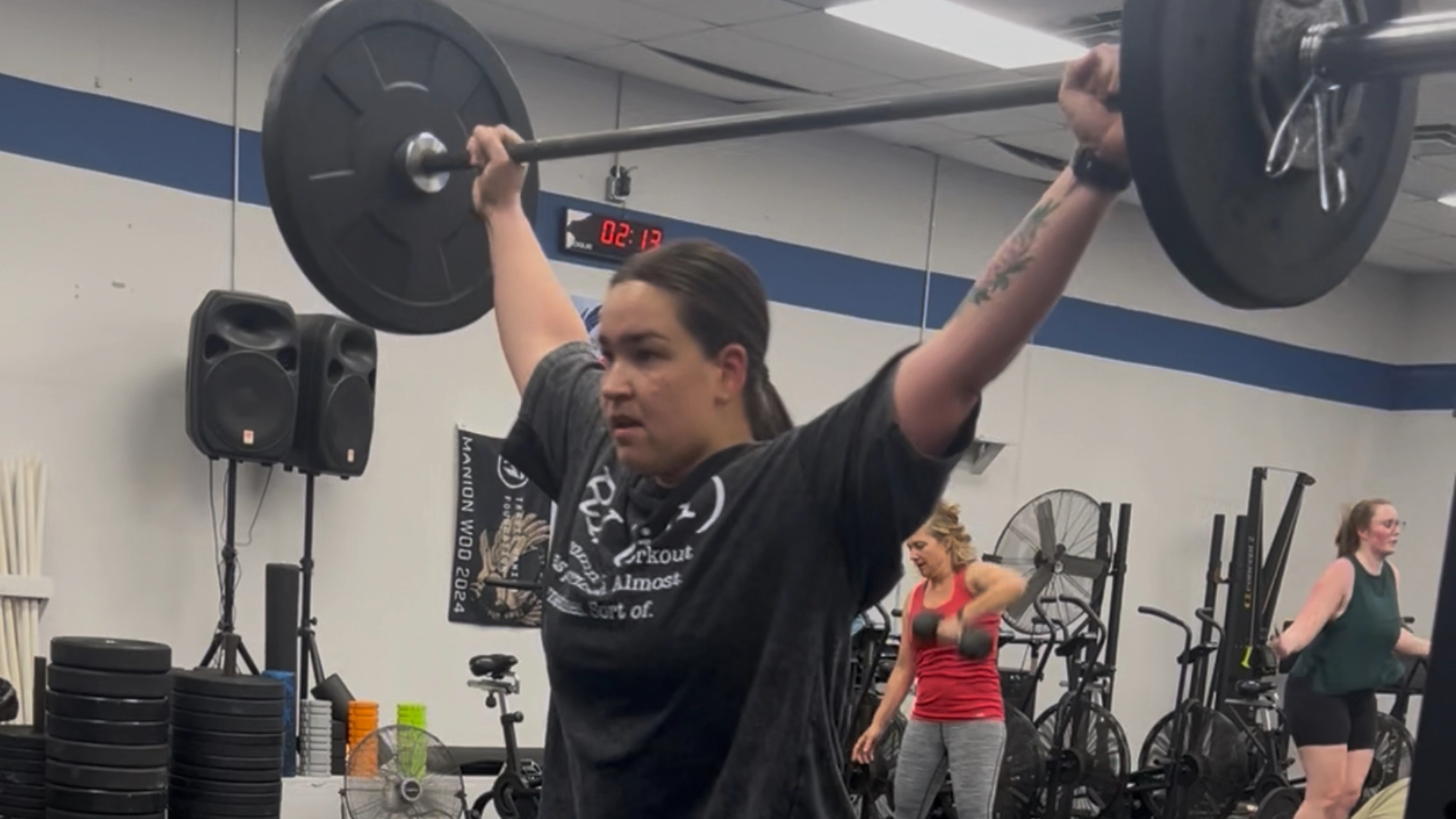 A woman lifts a barbell in a gym at CrossFit Empire South in Huntsville, AL, showcasing strength and determination.