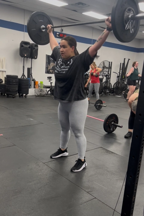 A woman lifts a barbell in a gym at CrossFit Empire South in Huntsville, AL, showcasing strength and determination.