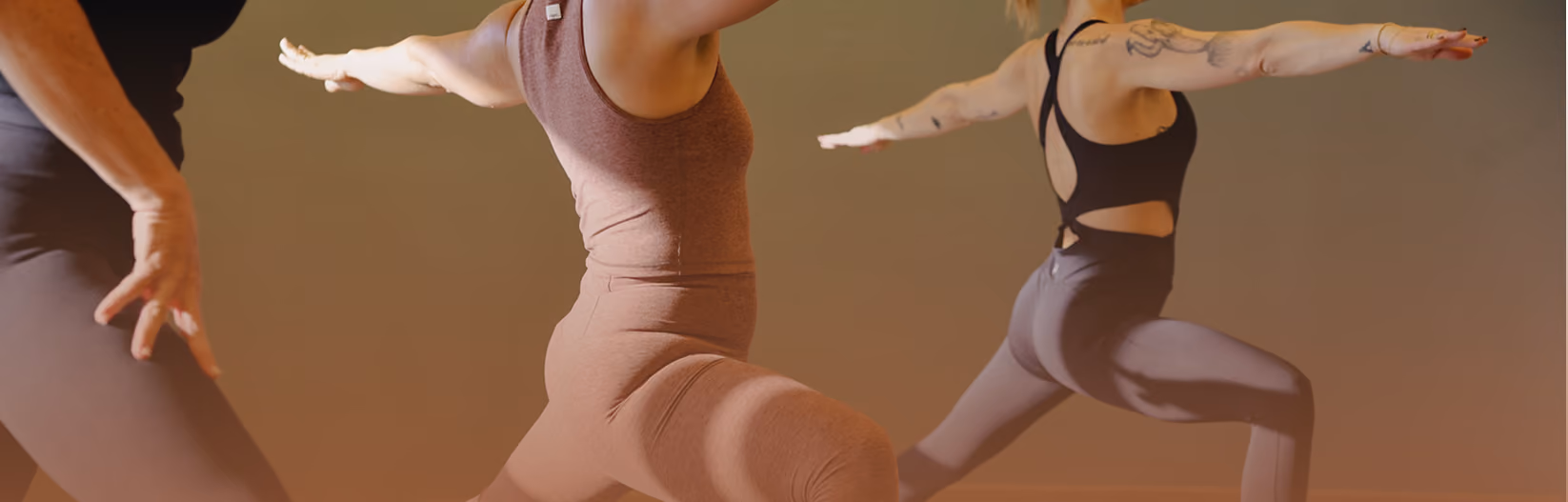 Three people in workout clothes practicing yoga in Warrior II pose indoors.