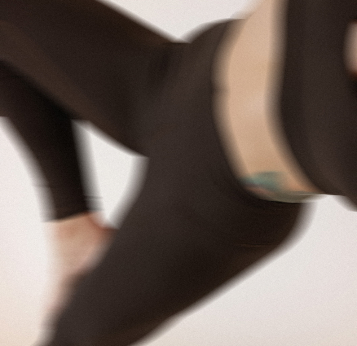 Blurred close-up of a person wearing black leggings and a black top, bending forward.
