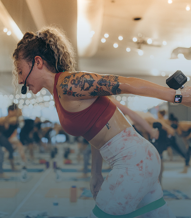 Female fitness instructor with headset and tattoos leading a workout class focused on resistance band exercises.