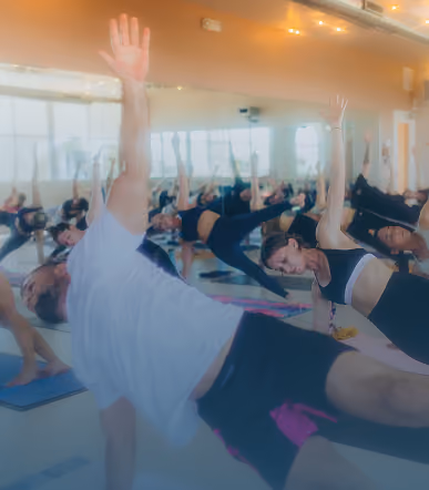 Group of people practicing side plank yoga pose in a bright studio with mirrored wall.