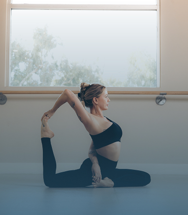 Woman in black workout clothes performing a yoga pose on the floor near a window.