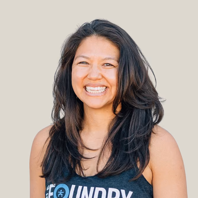 Smiling woman with long dark hair wearing a sleeveless shirt with The Foundry logo on a plain light background.