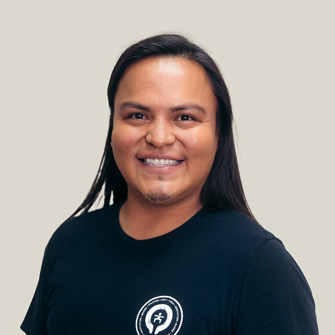 Smiling man with long dark hair wearing a black t-shirt with a circular logo, set against a plain light background.