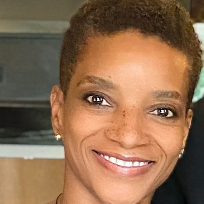 Close-up of a smiling woman with short curly hair, light freckles, and small earrings.