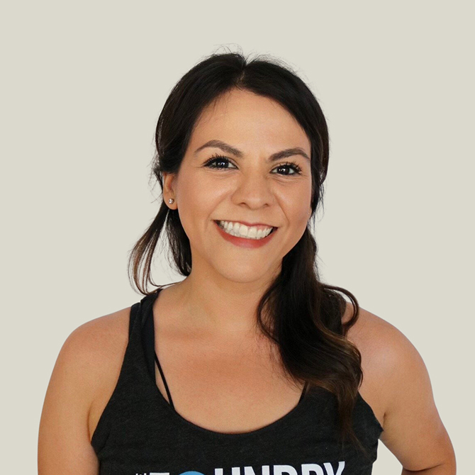 Smiling woman with dark hair wearing a black tank top against a light background.