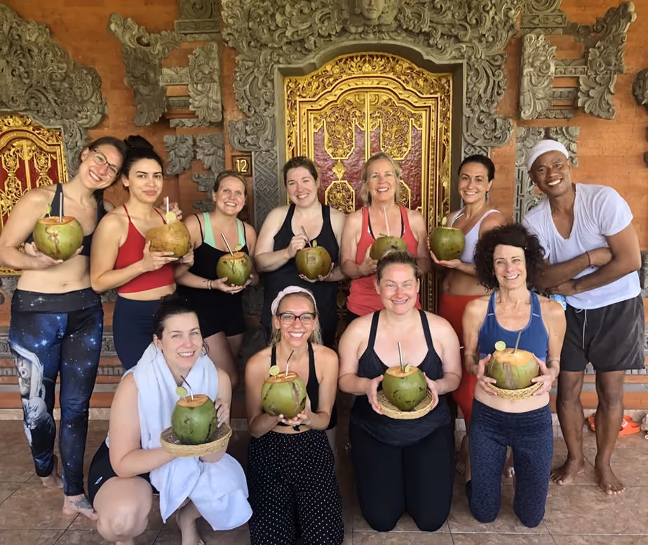 Group of eleven people smiling and holding coconuts with straws in front of ornate golden and stone carved doors.
