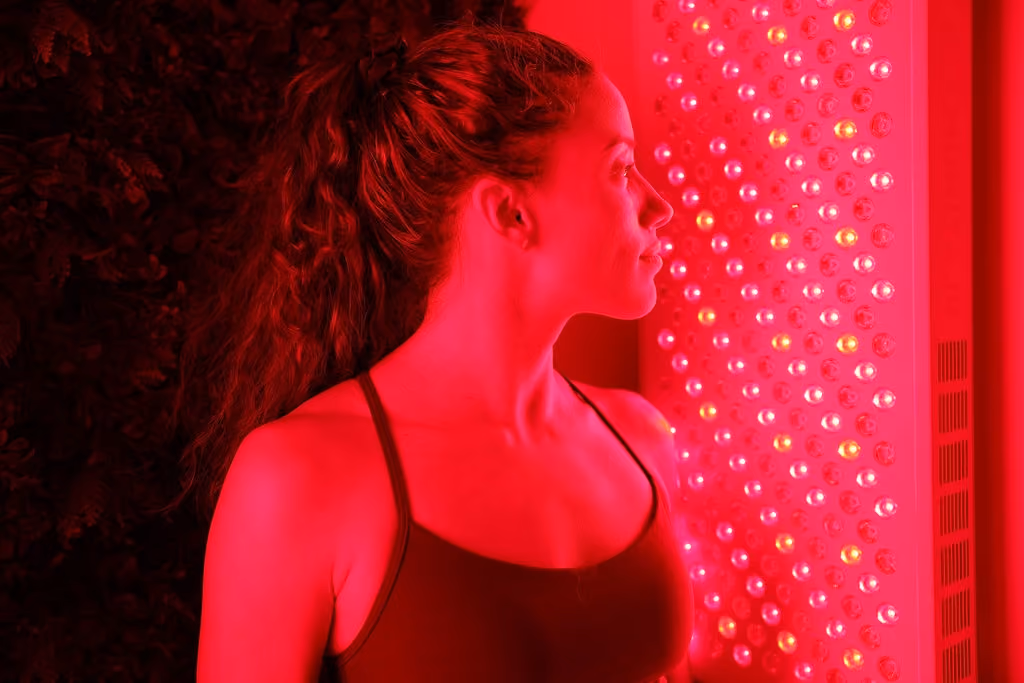 Woman in a tank top facing a light therapy panel glowing with red and yellow lights.