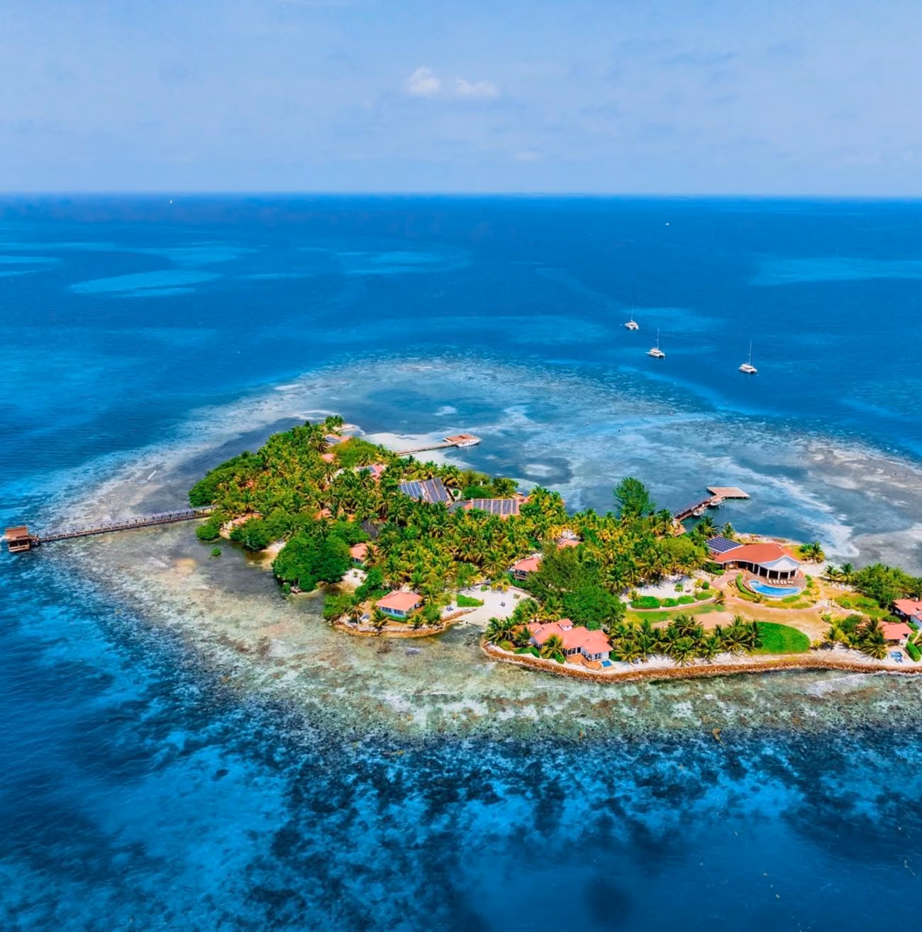 Aerial view of a lush tropical island with villas, docks, and boats in clear blue ocean waters.