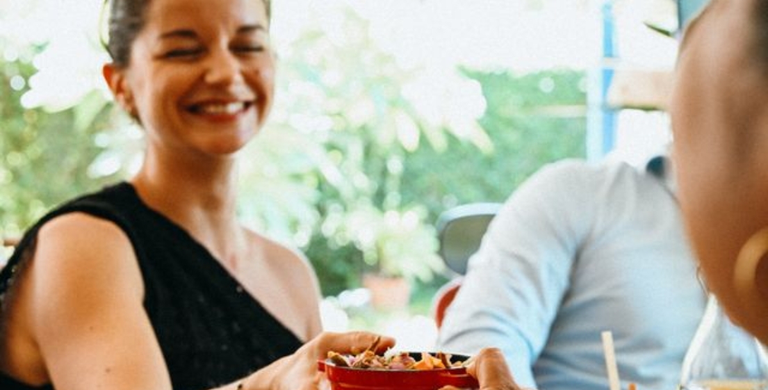 A person passing a dish with a smile during the Let's Eat & Play Together brunch in Mauritius, illustrating the spirit of sharing dear to MJ Holidays.
