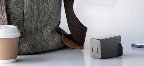 A coffee cup next to a gray backpack and a cuzor charger on a surface of the table.