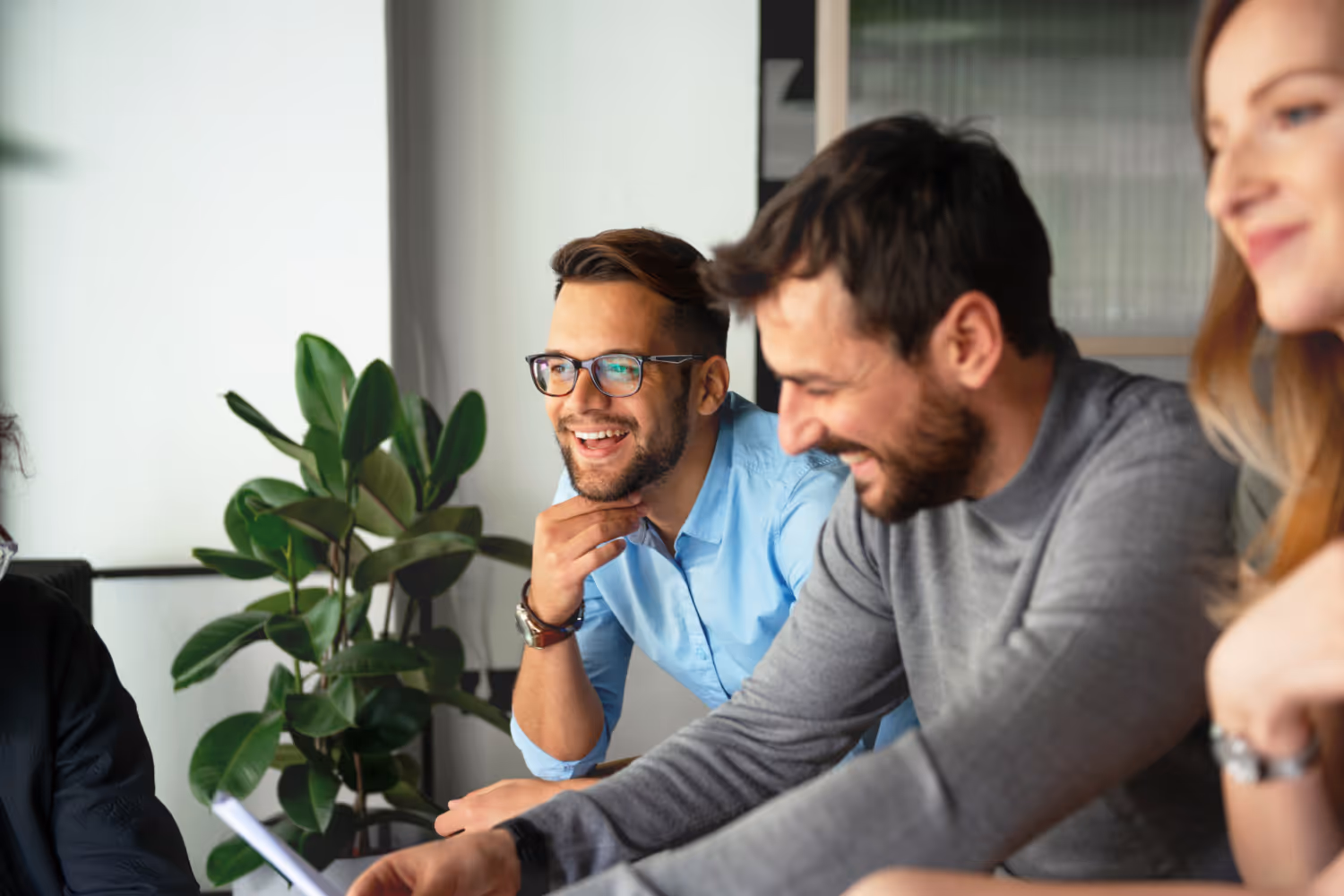Two men sitting at a table with a laptop and a potted plant.