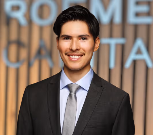 Smiling man in a dark suit and light gray tie standing in front of a blurred background with large text.