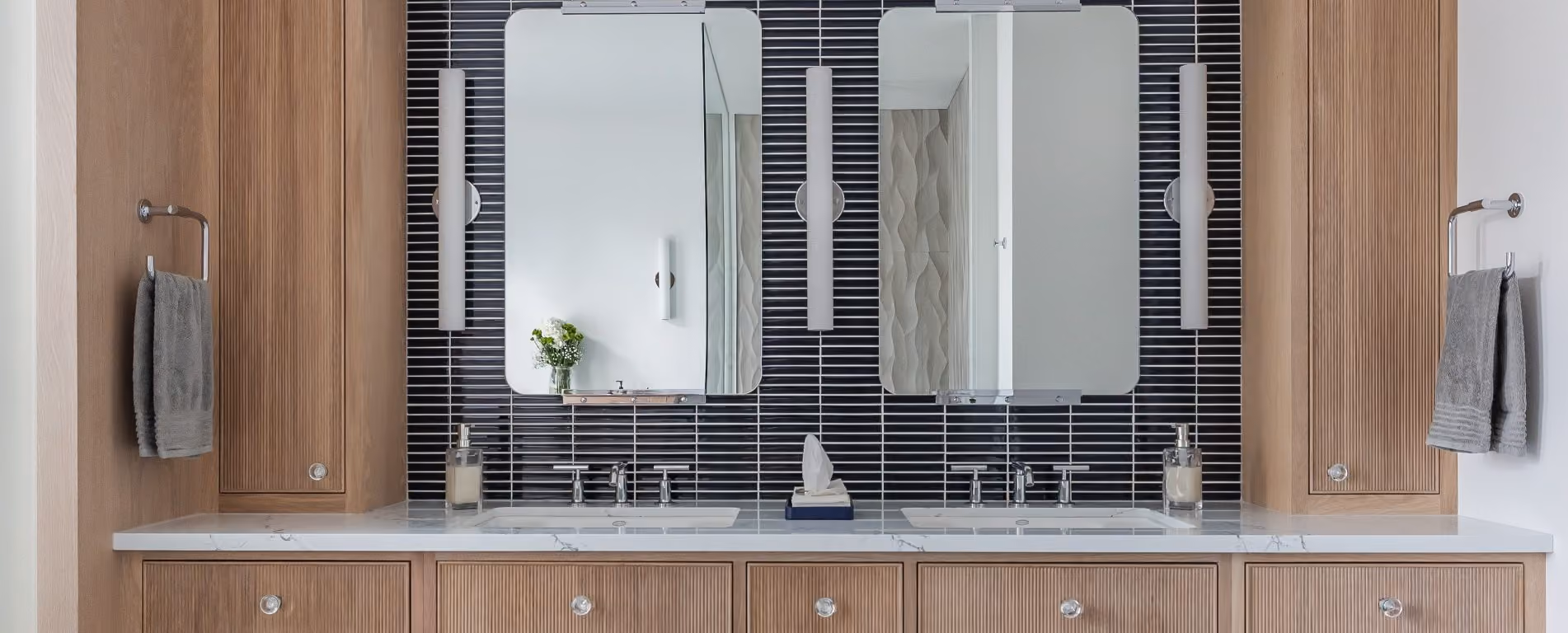 Modern double sink bathroom vanity with marble countertop, wooden cabinets, two mirrors, vertical lights, and grey hand towels.